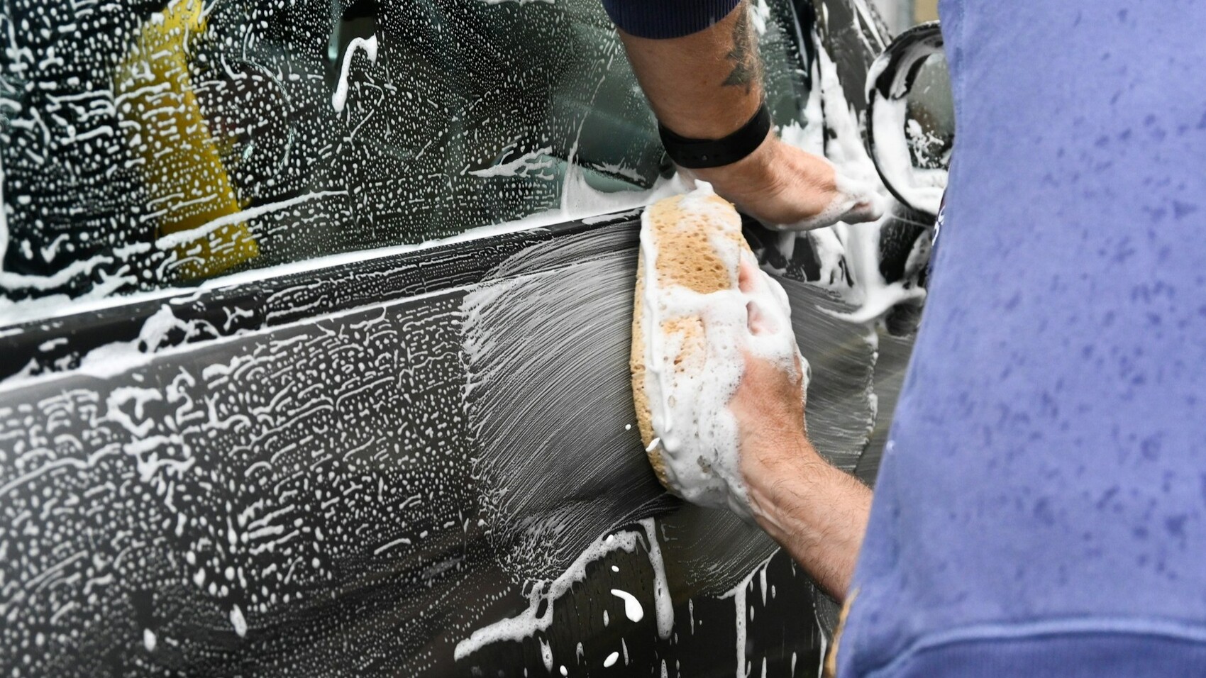 Man die buitenkant van een zwarte auto schoonmaakt met een spons en zeep