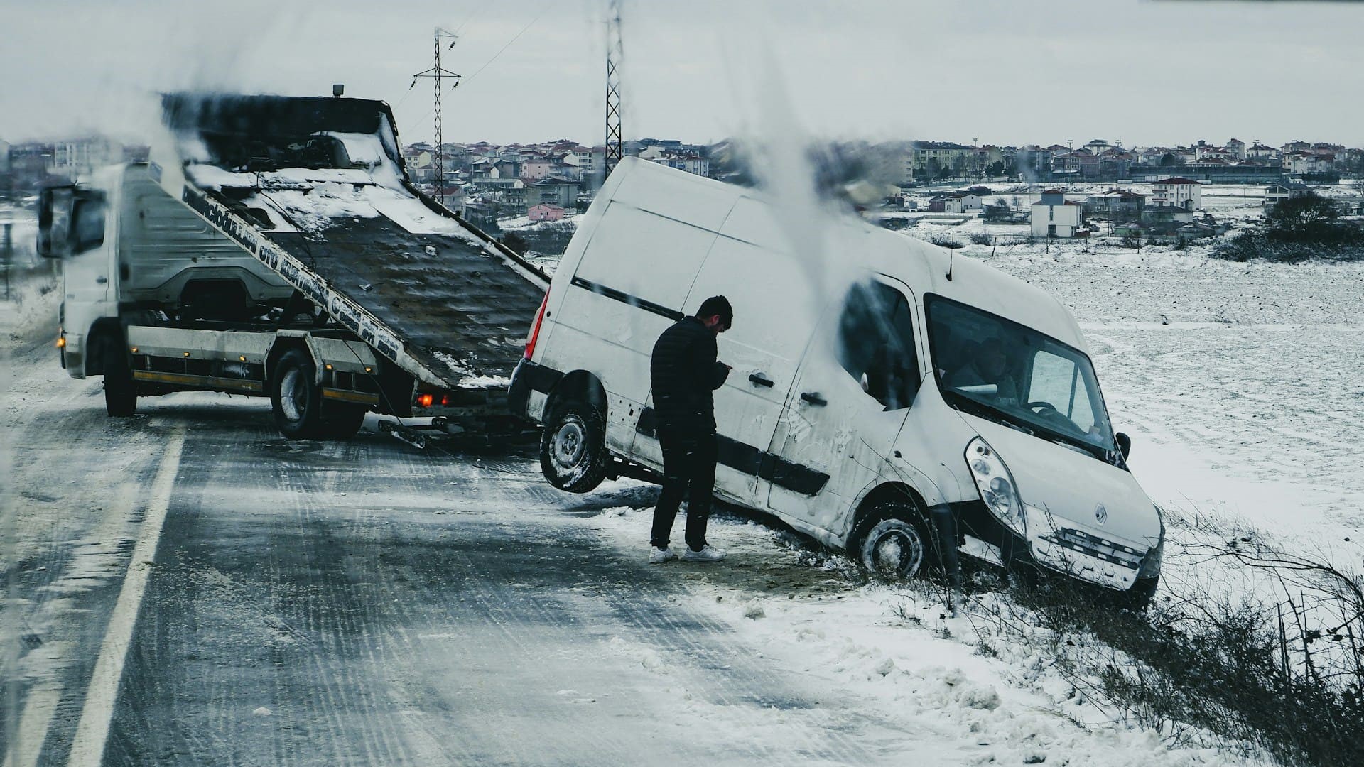 Verkeersincident met wit busje in de berm langs besneeuwde weg, sleepwagen gereed voor berging