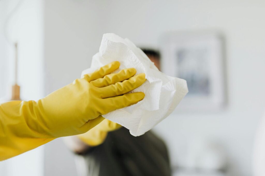 Hand met gele schoonmaakhandschoen houdt doek vast om oppervlak schoon te maken