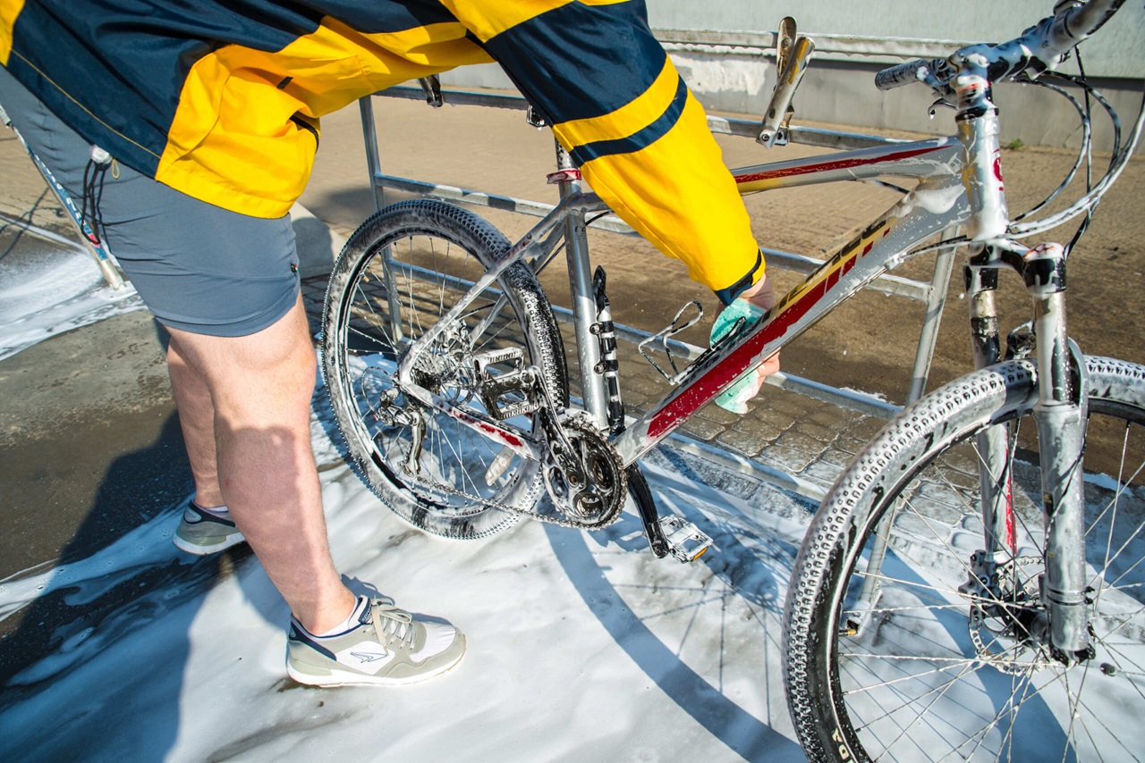 Persoon maakt een fiets schoon met een spons en zeep bij een wasplaats.