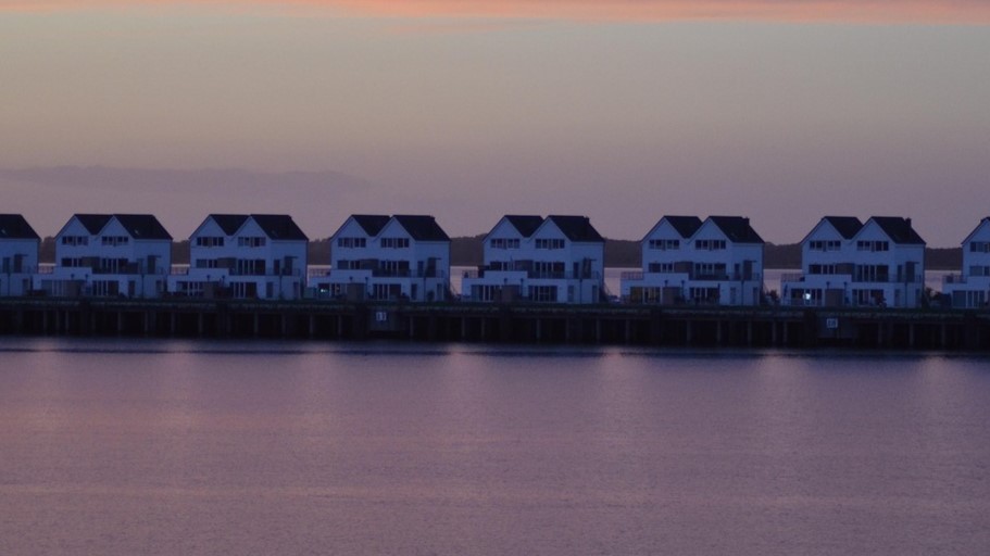 Rij moderne recreatieverblijven aan het water bij zonsondergang, weerspiegeld in een kalme paarse gloed