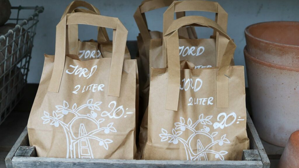 Papieren tassen met bedrukking “JORD 2 LITER” en witte boomillustratie in houten krat