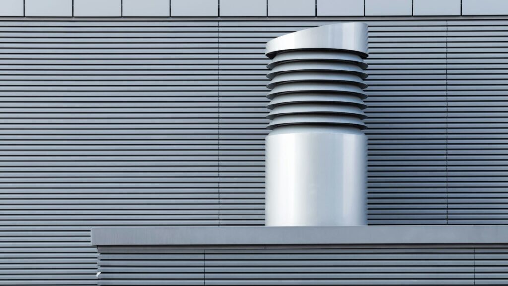 Moderne metalen ventilatie-unit tegen een gevel met horizontale lamellen, geschikt voor luchtcirculatie.
