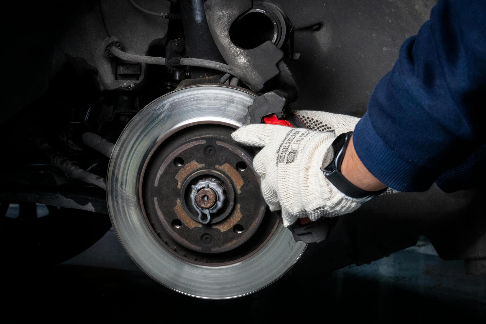 Monteur werkt aan remschijf van auto met handschoen en gereedschap
