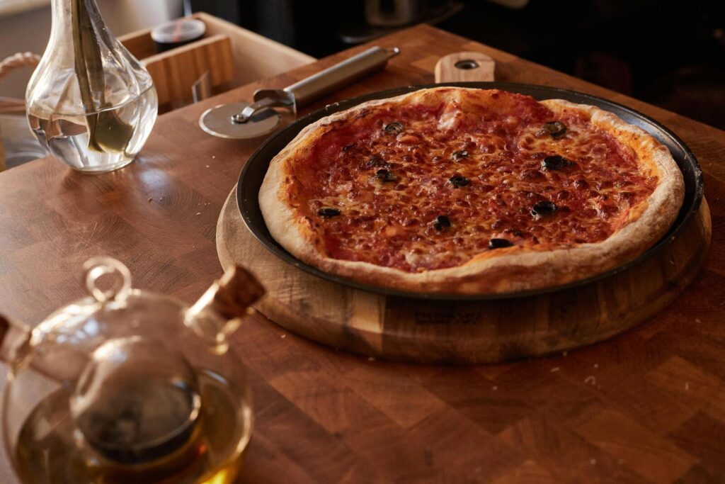 Pizza margherita ligt op houten plank op tafel met keukengerei ernaast