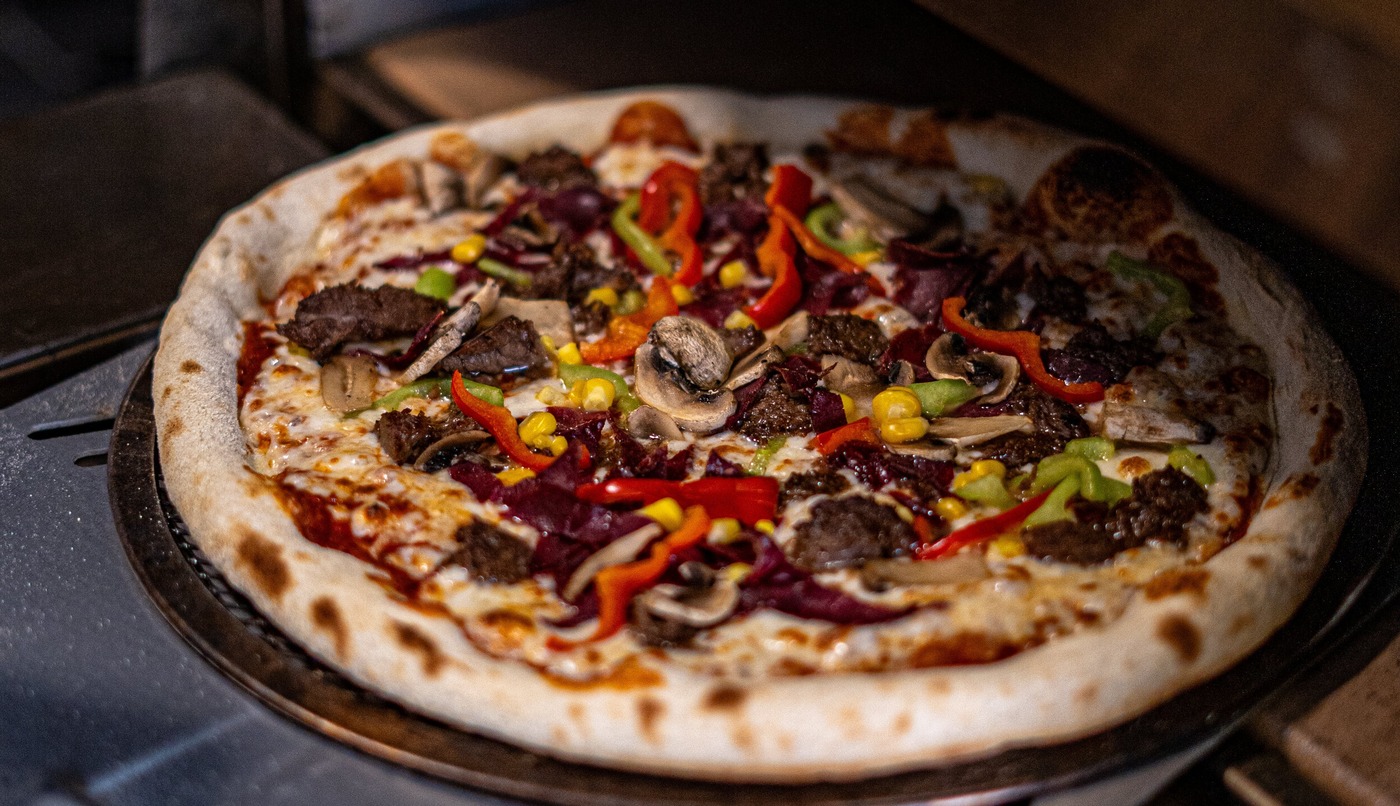 Pizza met vlees, paprika en ui ligt op houten plank