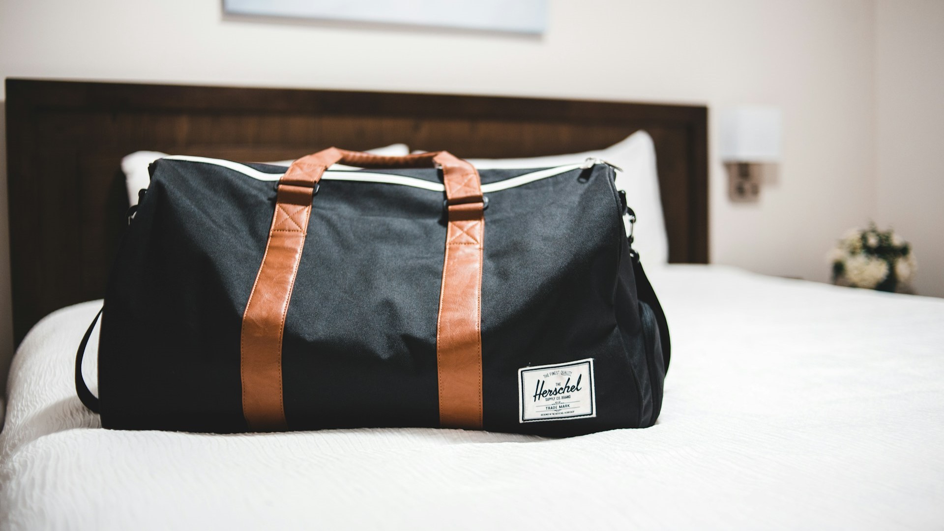 Zwarte sporttas met bruine hengsels staat schoon en netjes op een wit opgemaakt bed – sporttas schoonmaken