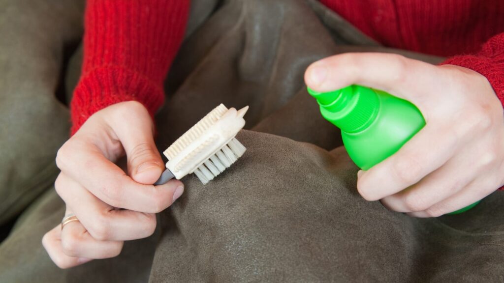 Handen spuiten reinigingsmiddel op bank met borstel – gericht vlekken verwijderen op textiel
