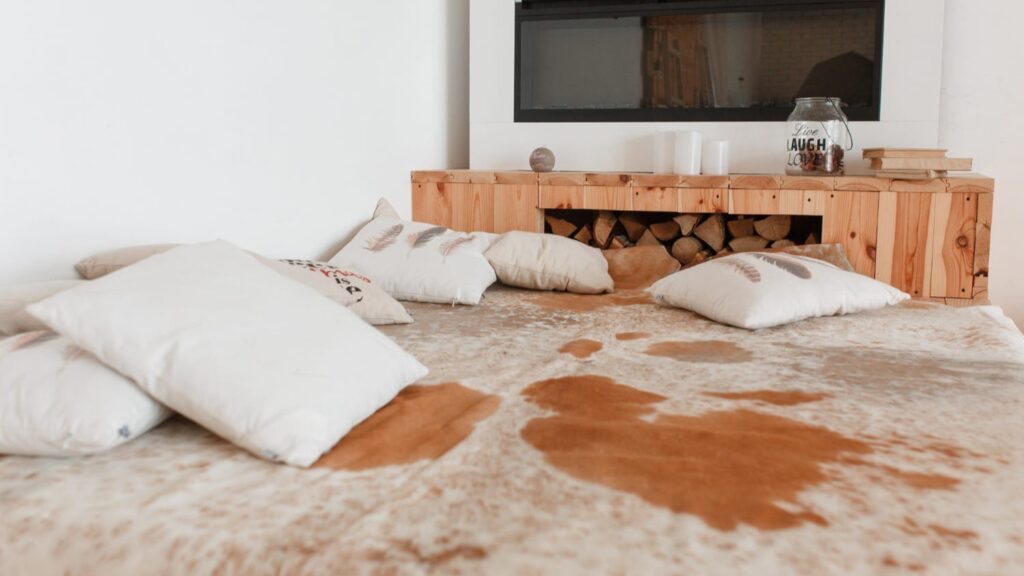 Grote vetvlekken op een licht vloerkleed met verspreide kussens – vlekken verwijderen vereist snelle actie