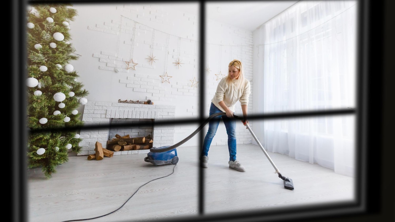Voorjaarsschoonmaak in woonkamer met stofzuiger terwijl kerstdecoratie wordt opgeruimd na de winter